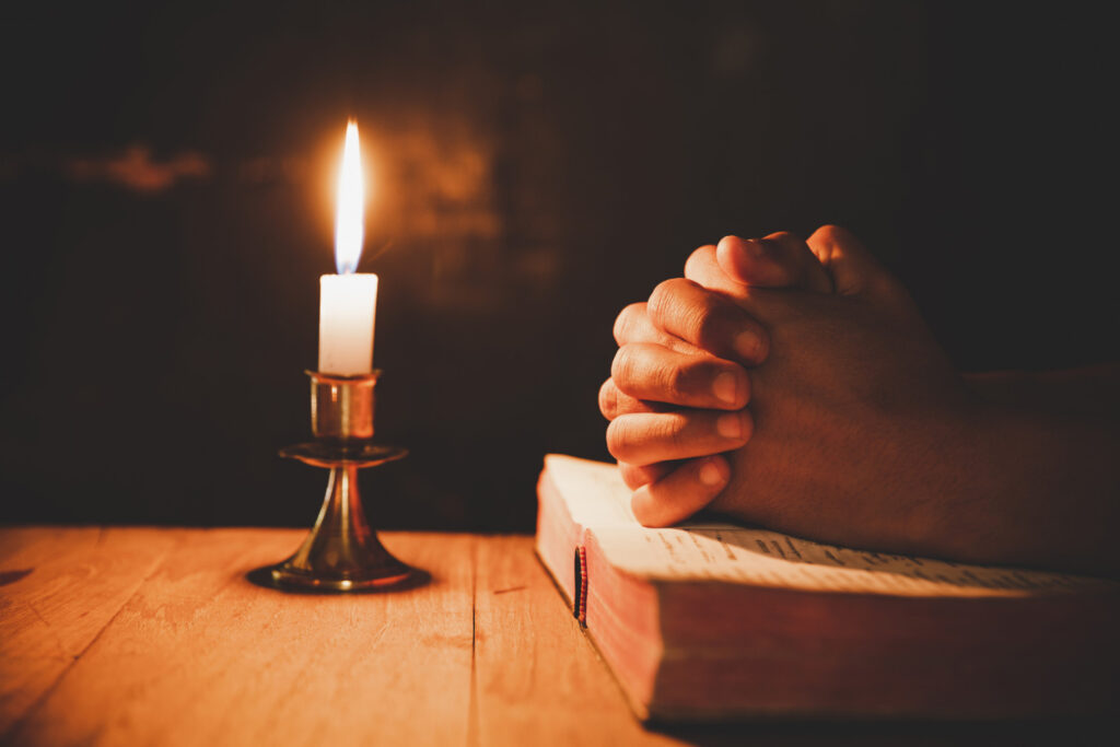 man praying bible light candles selective focus